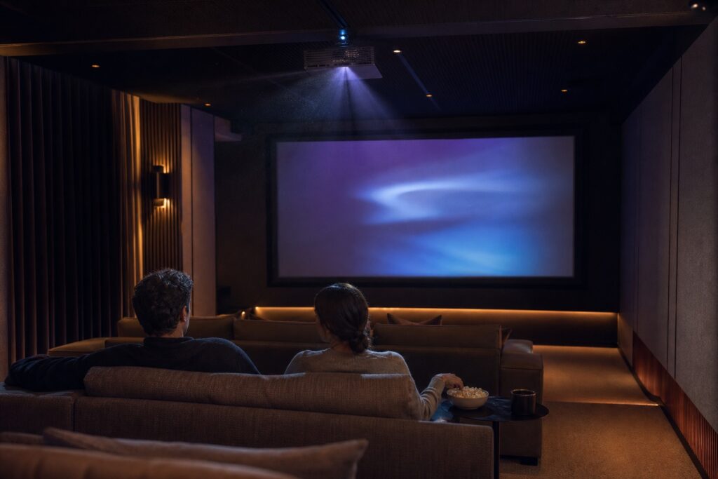 Two people using a quiet home cinema with an abstract image on screen.